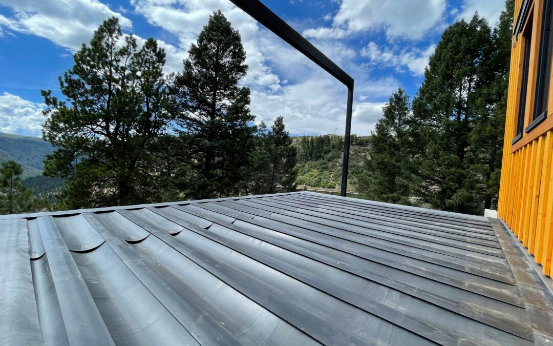 A photo of DEK Drain's rubber membrane system during installation set against a blue sky and towering pines for rubber or plastic under-deck drainage blog.