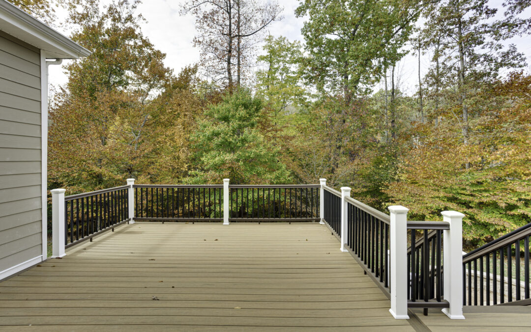 A spacious wooden deck attached to a house, bordered by a simple railing and overlooking a vibrant autumn forest for new-deck-vs-existing-deck blog.